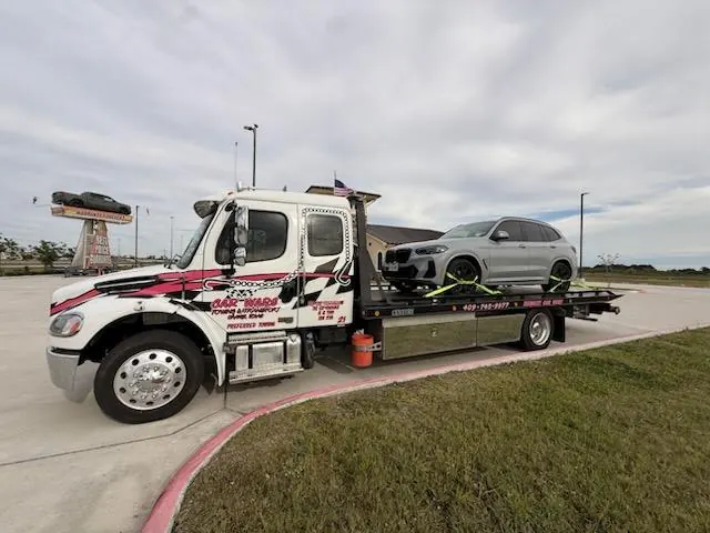 White Car Wars flatbed tow truck with secured BMW X3 SUV in Orange, Texas