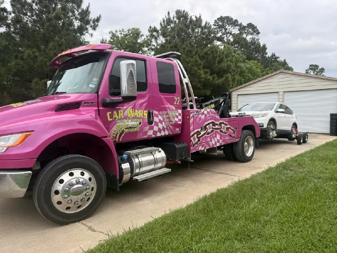 Pink Car Wars flatbed wrecker towing a BMW X7 SUV from a residence in Orange, TX
